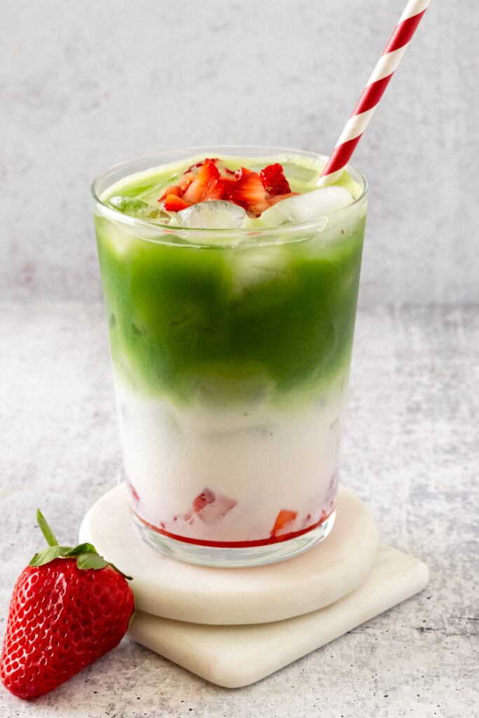 This Strawberry Matcha Latte is layered in a cup with fresh strawberry puree, milk, matcha and garnished with more strawberries.