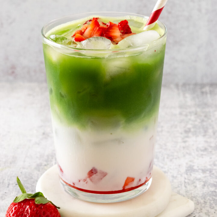 This Strawberry Matcha Latte is layered in a cup with fresh strawberry puree, milk, matcha and garnished with more strawberries.