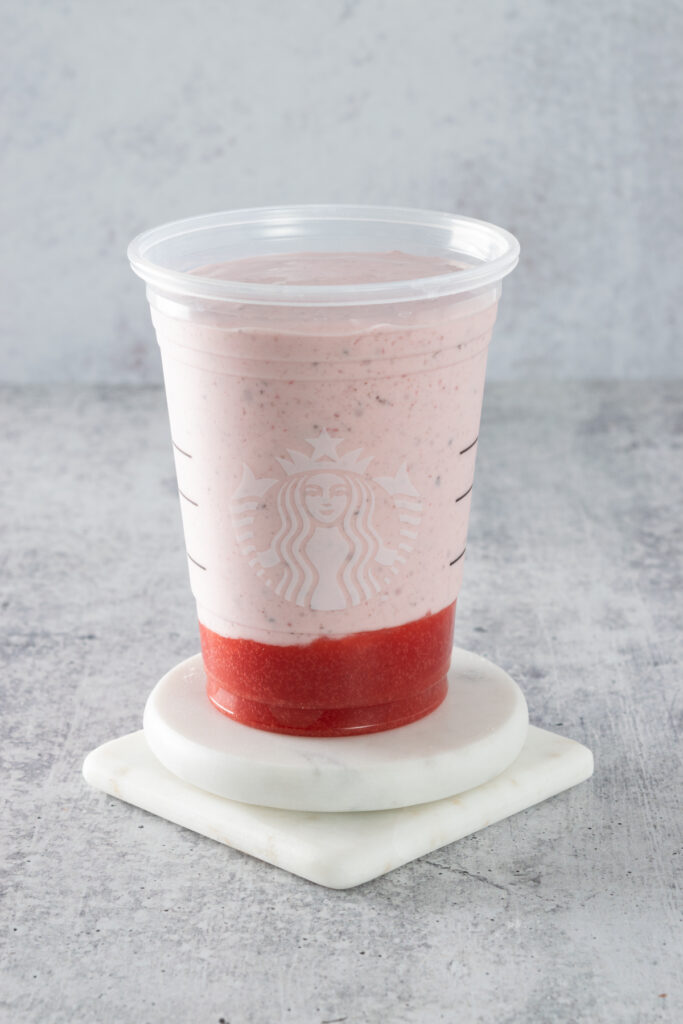 Blended frappuccino poured on top of the puree inside the Starbucks cup.