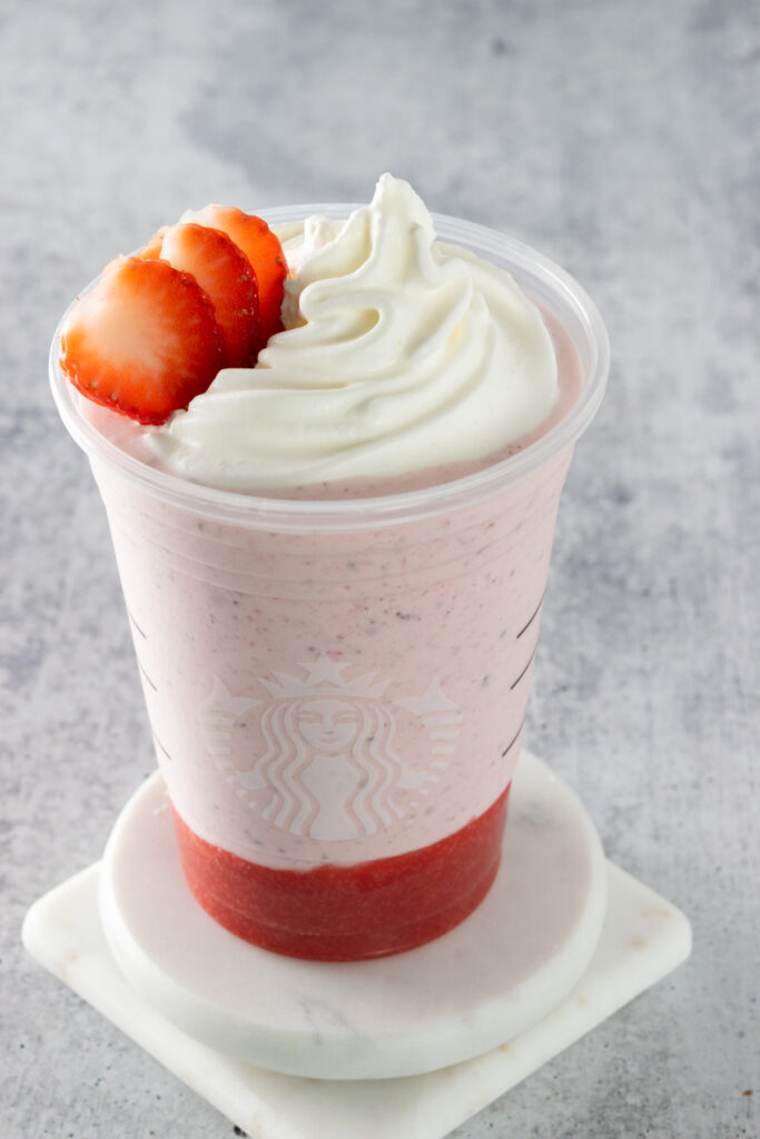 Chocolate-covered strawberry frappuccino in a Starbucks cup, topped with whipped cream and garnished with slices of fresh strawberry.