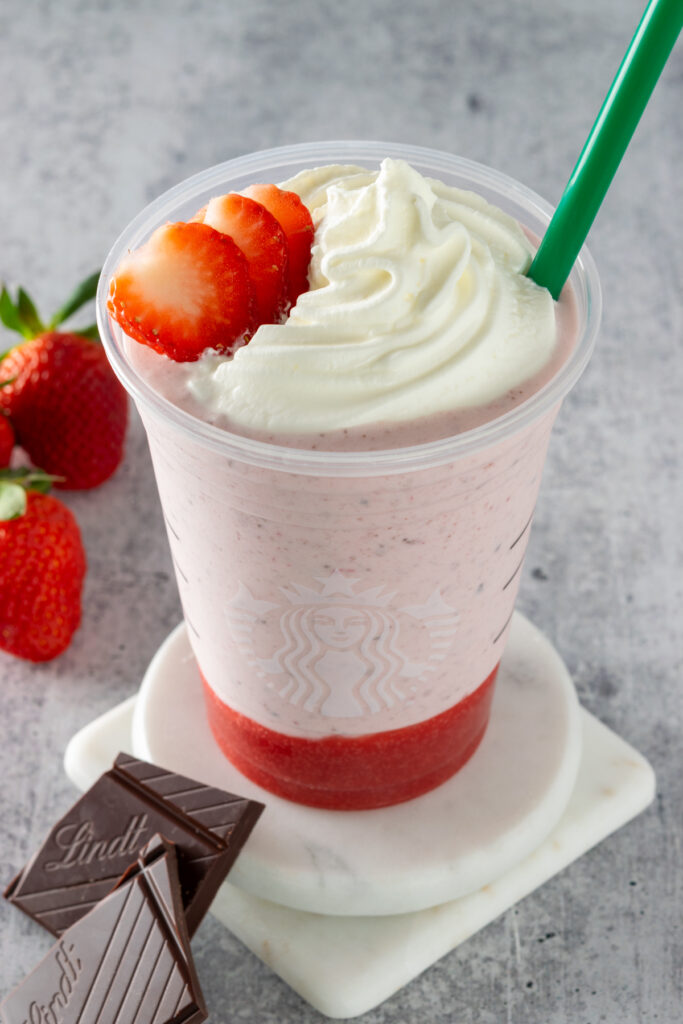 A homemade chocolate-covered strawberry frappuccino in a Starbucks cup with sliced strawberries and whipped cream on top.