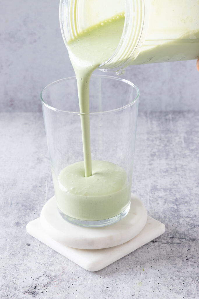 Pouring a banana matcha smoothie into a drinking cup.