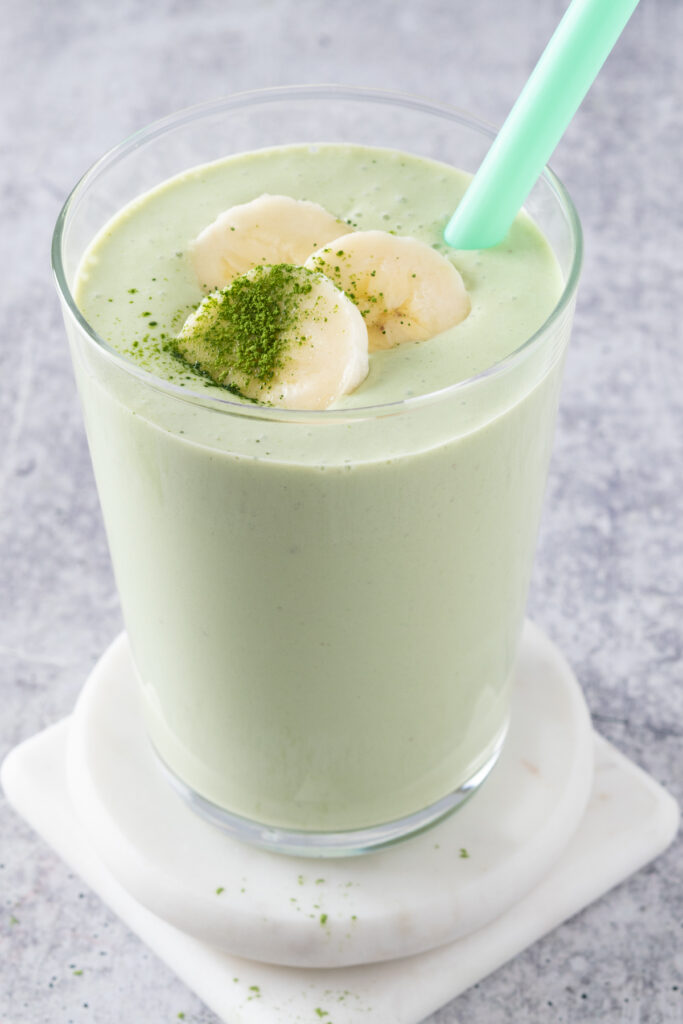 A blended matcha smoothie that's topped with slices of banana and a little bit of matcha powder sprinkled on top.