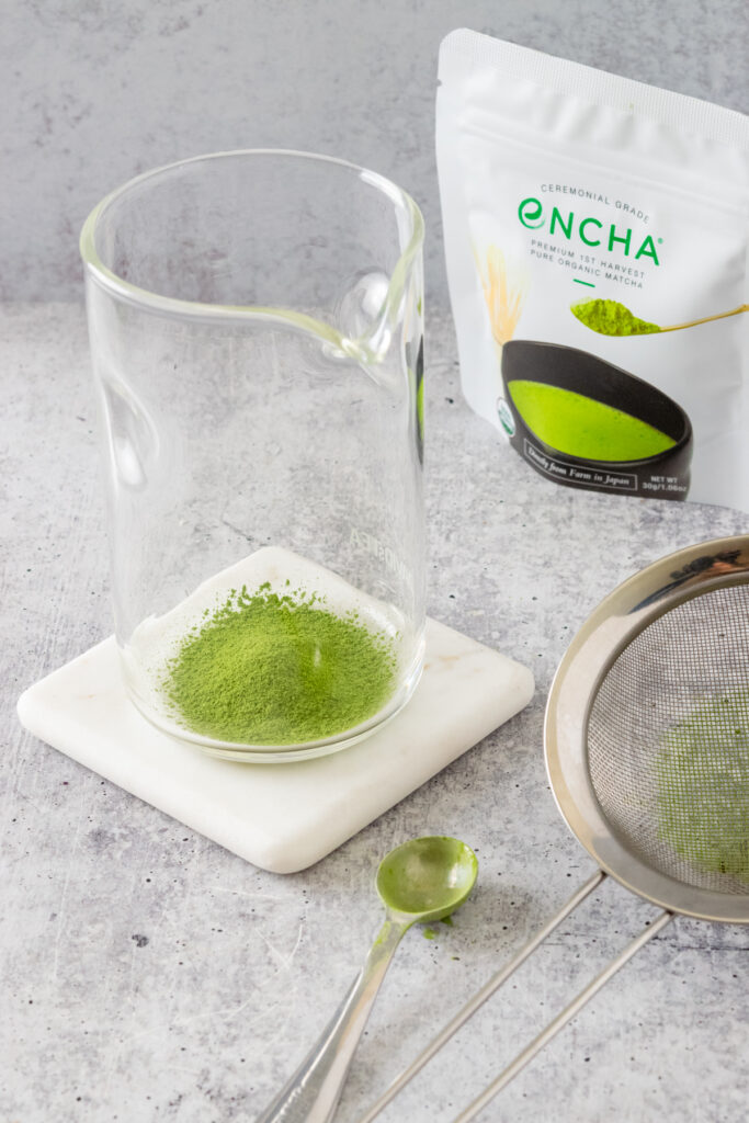 Sifted matcha in a bowl sitting in front of a bag of matcha green tea poweder.