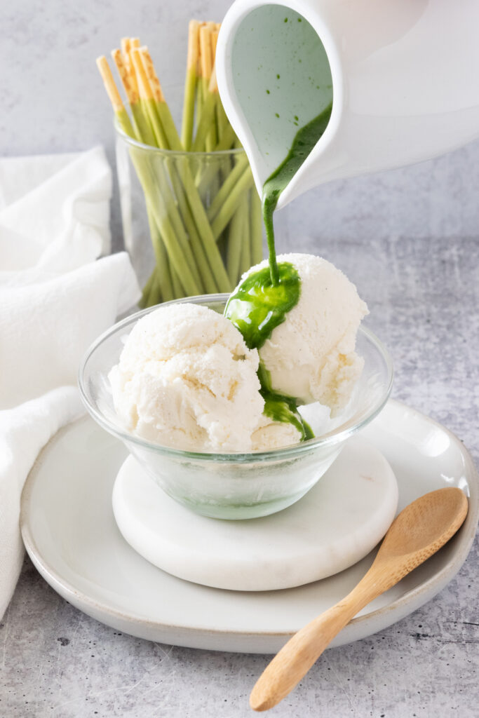 Matcha green tea being poured over scoops of vanilla ice cream in a small bowl to make a matcha affogato.