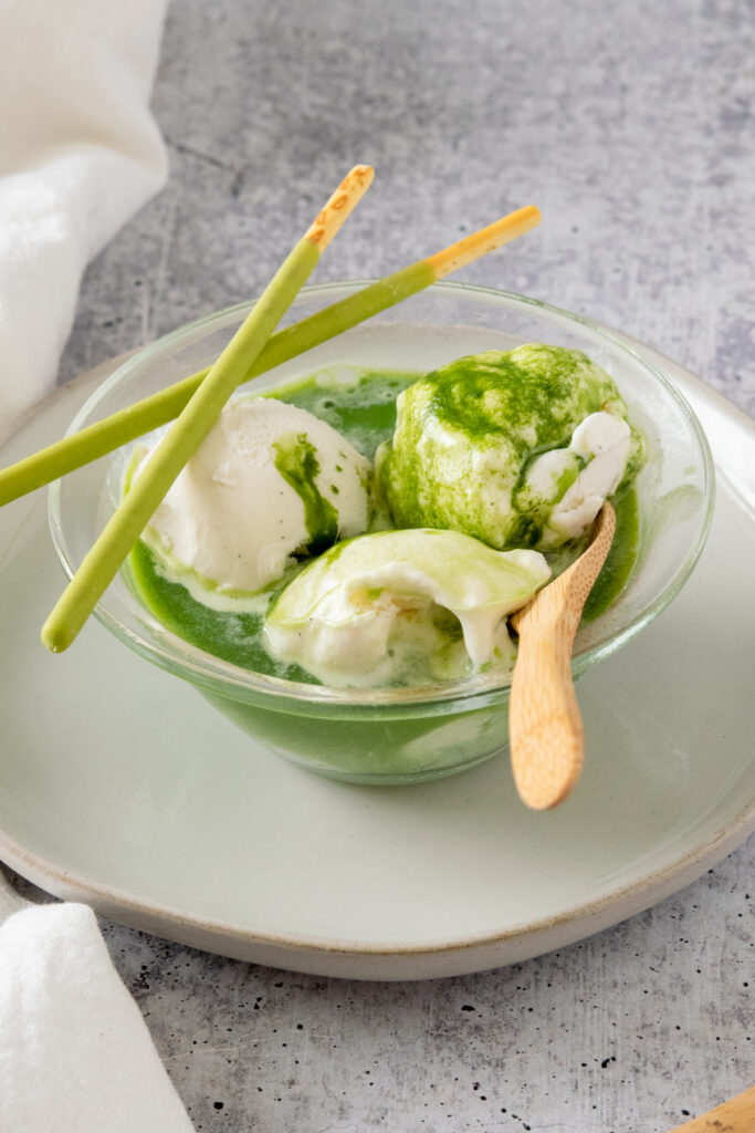 Matcha affogato in a bowl with two matcha green tea cream Pocky sticks as a garnish.
