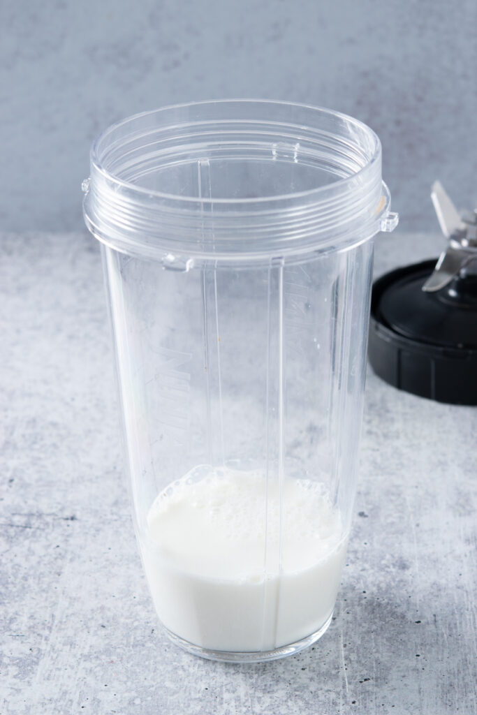 Milk in a blender cup with the screw on blade in the background.