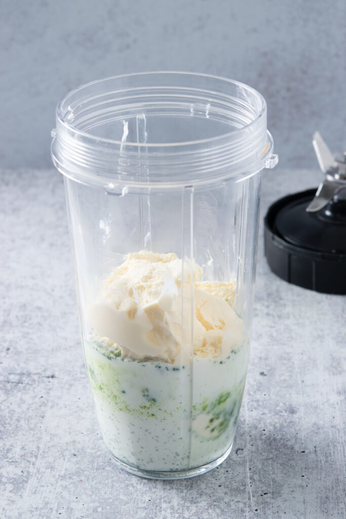 Vanilla ice cream added to blender cup on top of matcha and milk.