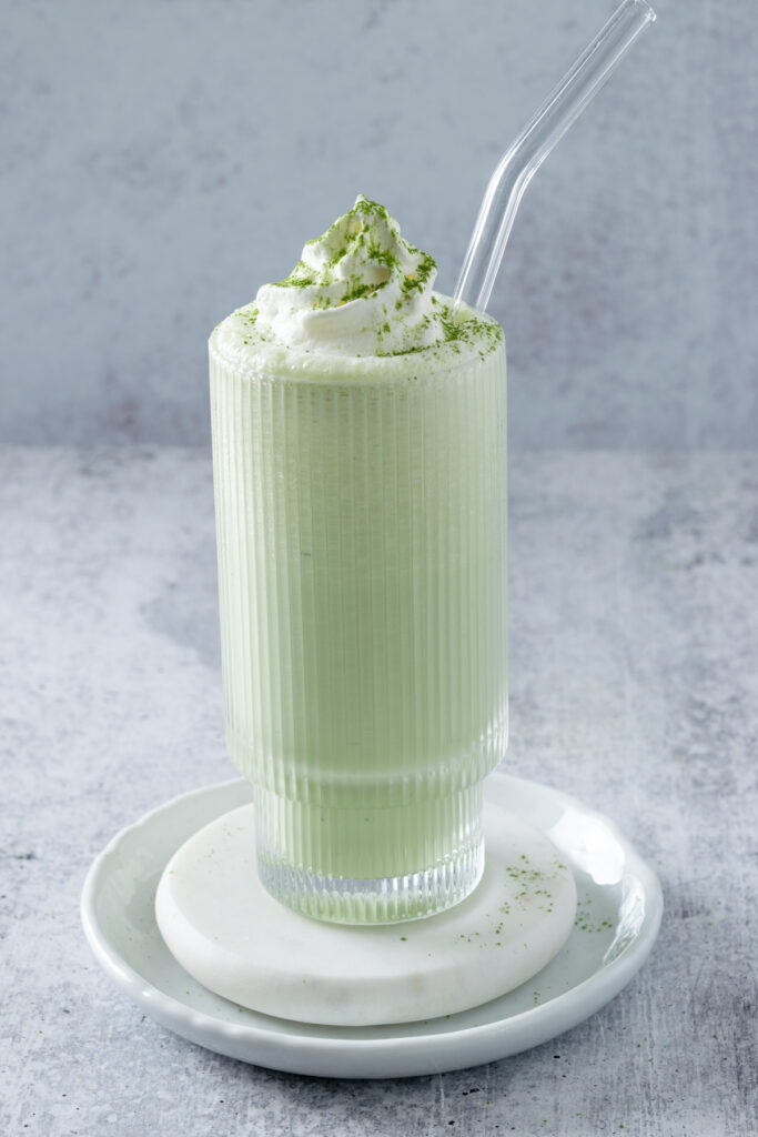 Matcha milkshake with dollop of whipped cream and sifted matcha powder on top.