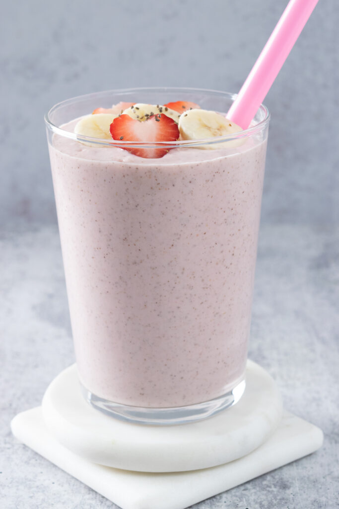 A strawberry banana smoothie with chia seeds in it with a pink straw sticking out of the glass cup.