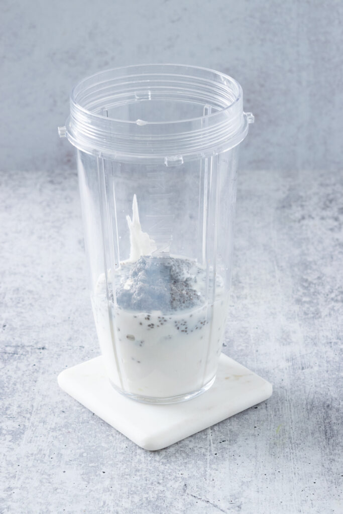 Soaked chia seeds and milk poured on top of the yogurt in a blender cup.