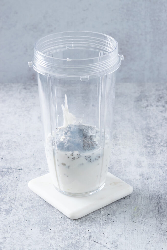 Soaked chia seeds and milk poured on top of the yogurt in a blender cup.
