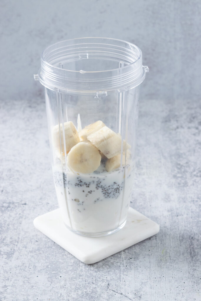Ripe banana added to a blender cup that has yogurt, chia seeds and milk in it.