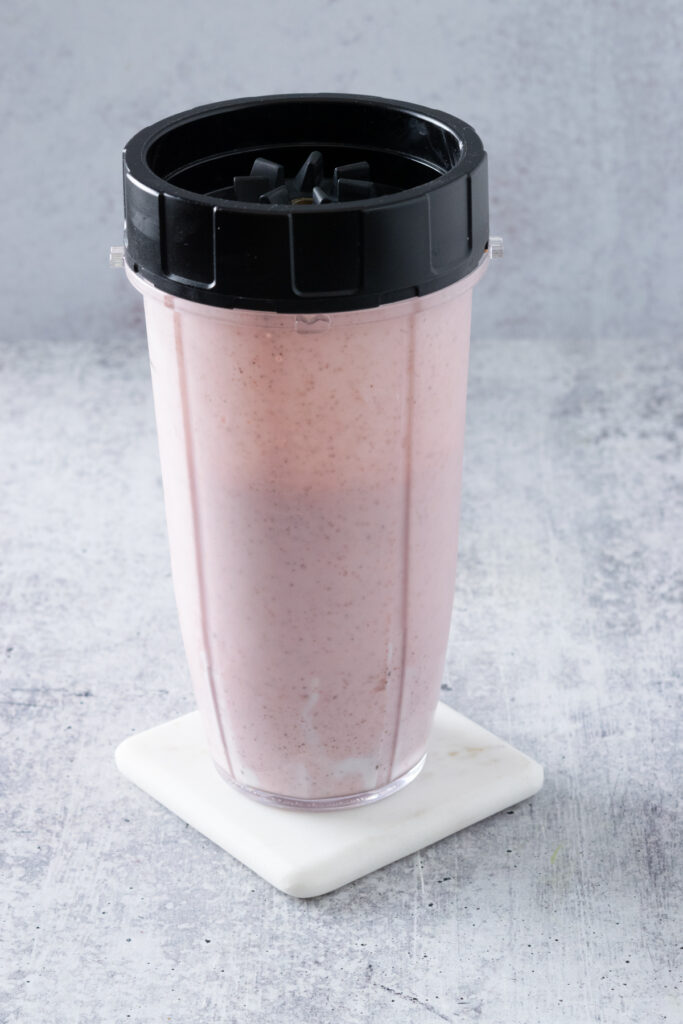A pink, blended strawberry banana smoothie in a blender cup.