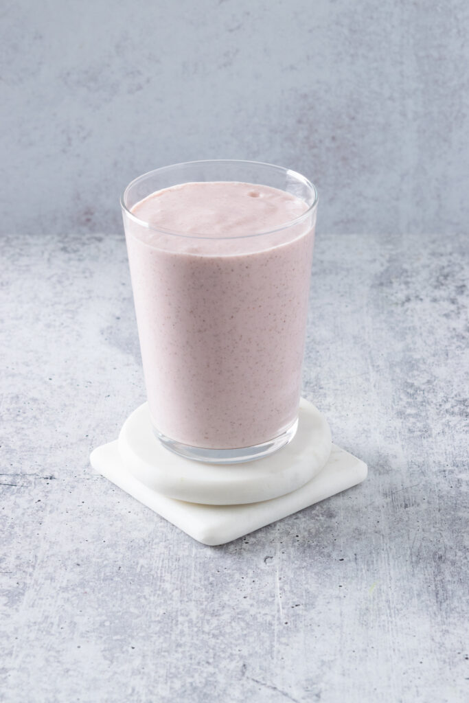 A homemade strawberry banana smoothie poured into a glass showing its pretty pink color.