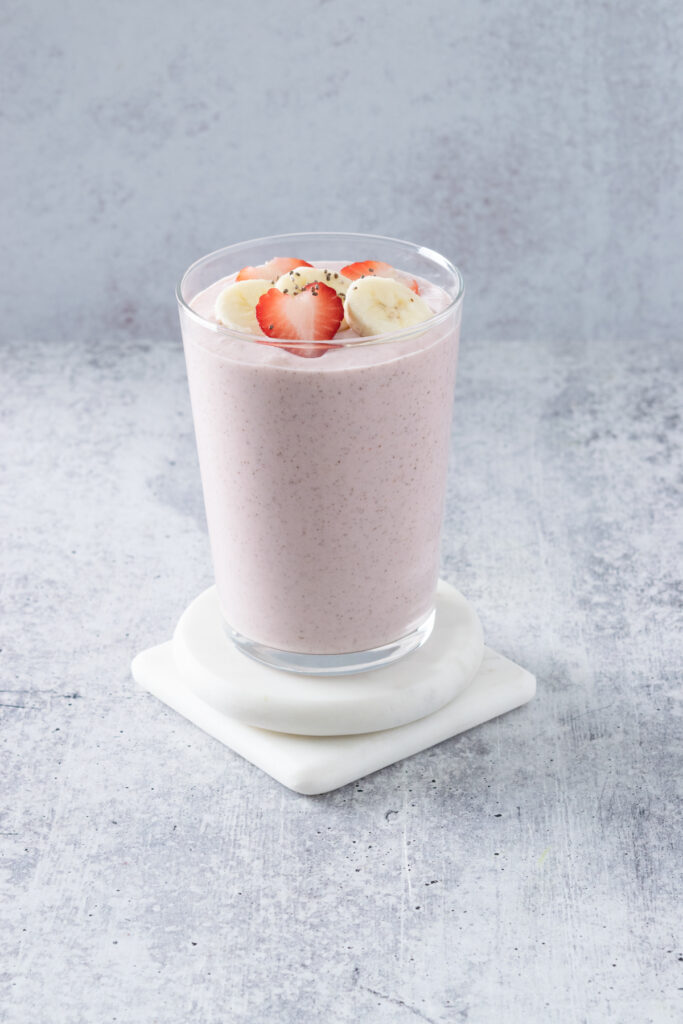 A homemade chia seed strawberry banana smoothie poured in a glass showing the pink smoothie. The drink is topped with a few slices of fruit with a few chia seeds sprinkled on.