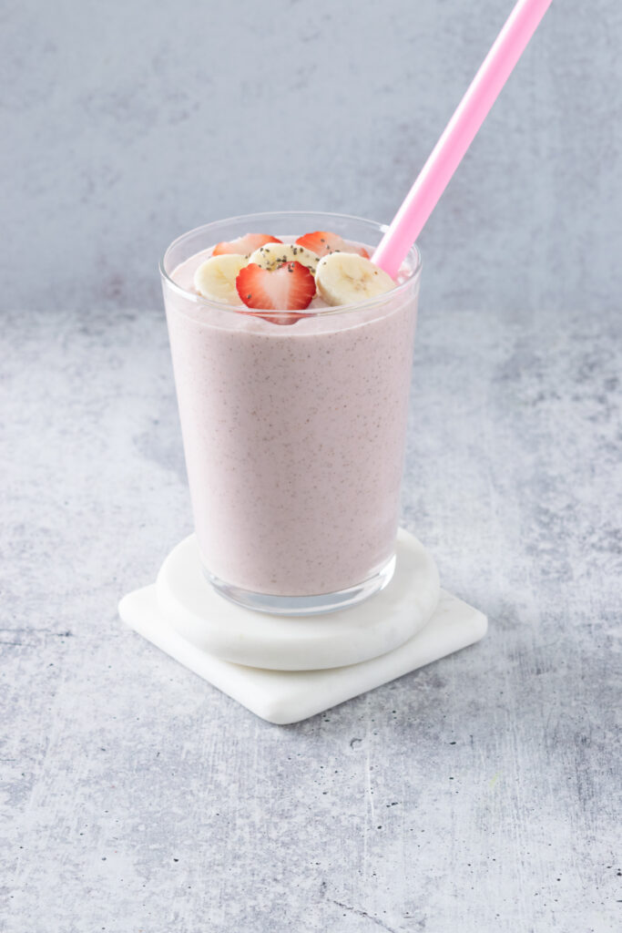 Strawberry Banana Chia Seed Smoothie with a pink straw in it, in a glass cup showing all the seeds in the pink colored smoothie.