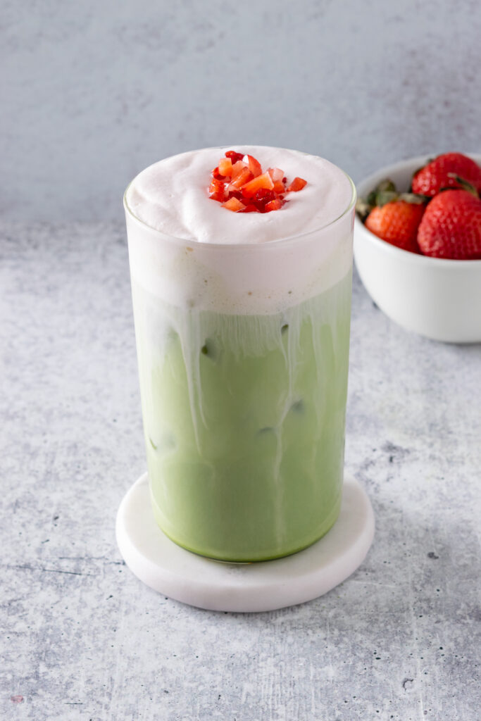 The finished iced strawberry cream matcha latte garnished with chopped strawberries on top of the cold foam.