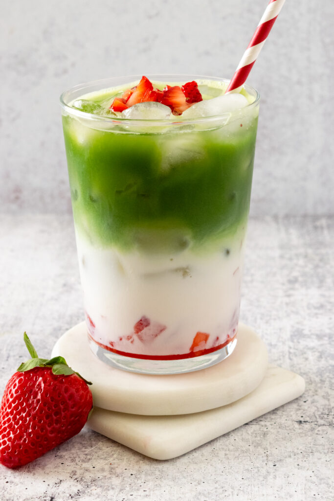An aesthetic matcha strawberry latte with three colored layers in a glass sitting next to a strawberry.