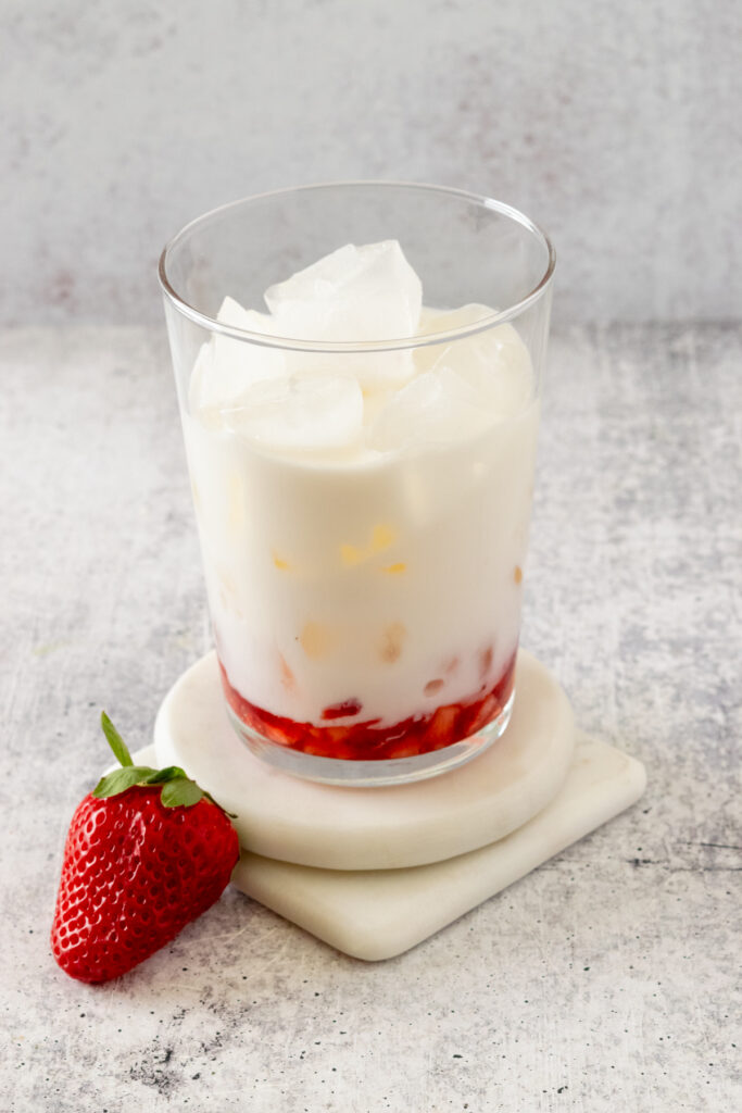Milk poured into glass with ice and strawberries.