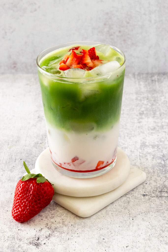 A strawberry matcha latte garnished with chopped, fresh strawberries.