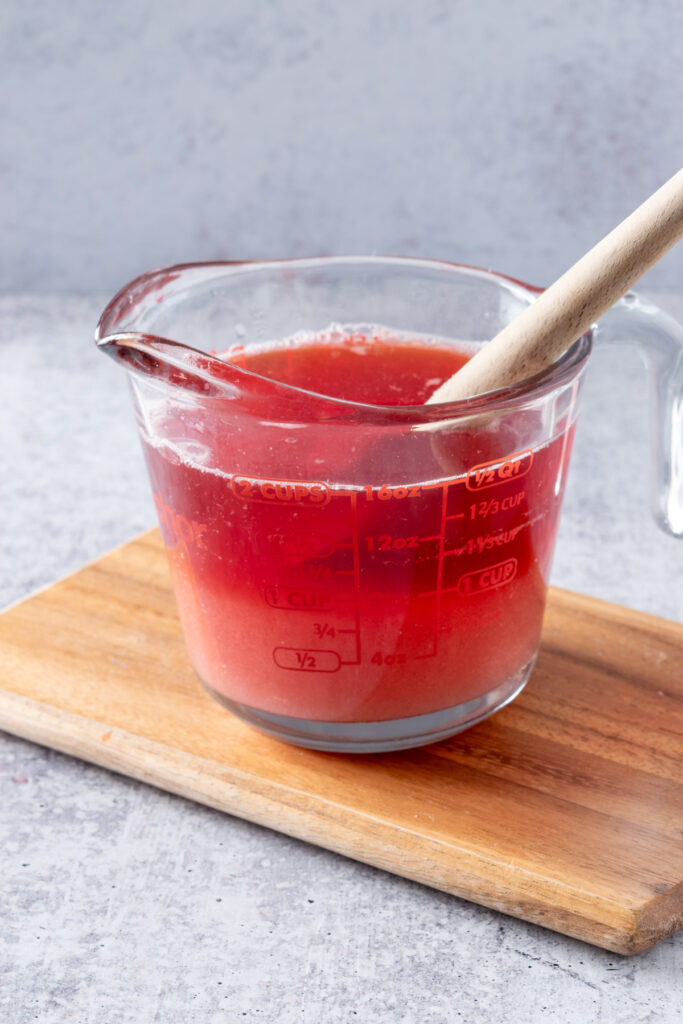 A glass measuring cup with strawberry juice and sugar poured into it.