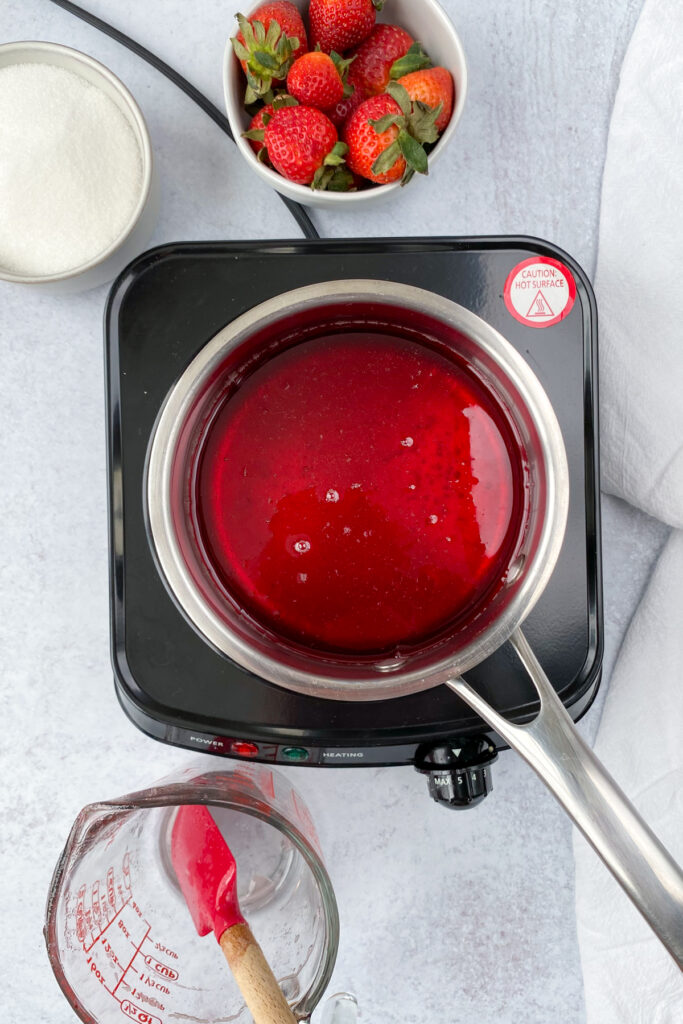 Strawberry syrup in a saucepan on a burner being boiled to dissolve all the sugar.