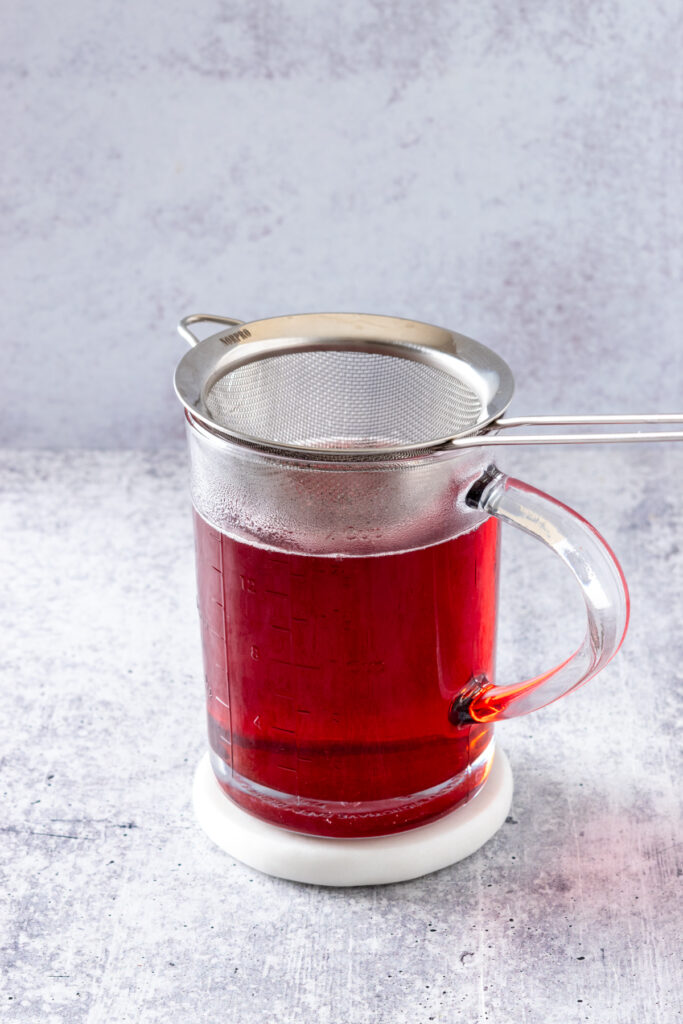 Homemade strawberry simple syrup poured into a container with a small fine mesh strainer on top.