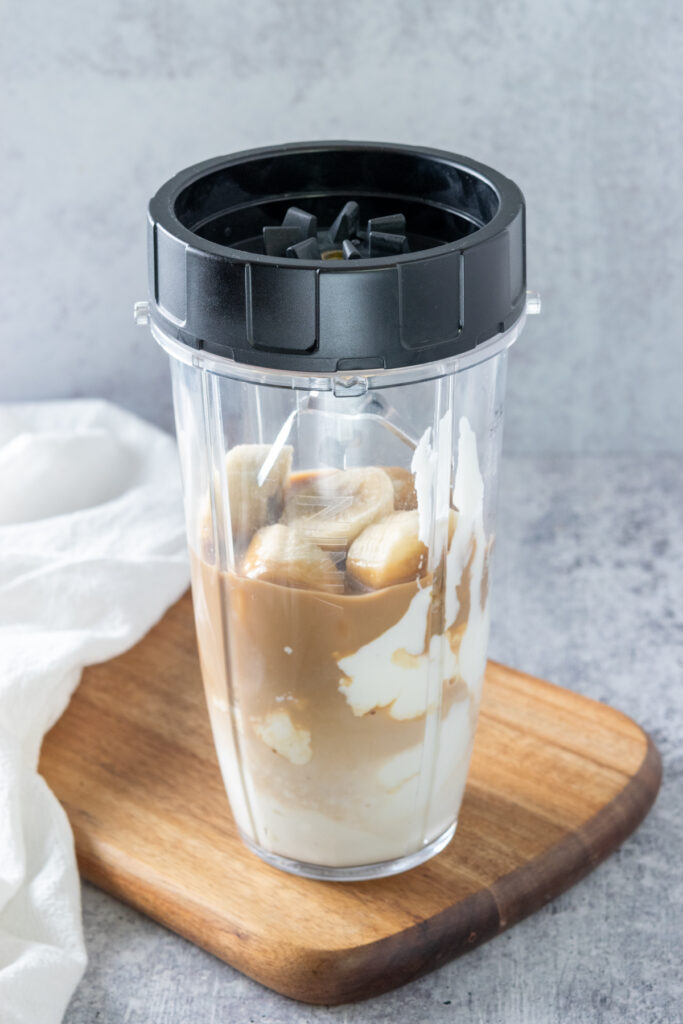 Ninja single-serve blender container with smoothie ingredients in it and lid with blades screwed on top.