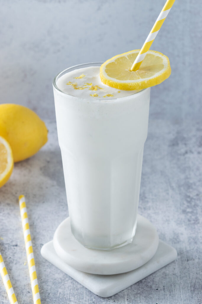 Frosted lemonade poured into a frosty cup that's been chilled in the freezer. The lemonade is topped with zest and a slice of lemon to garnish.