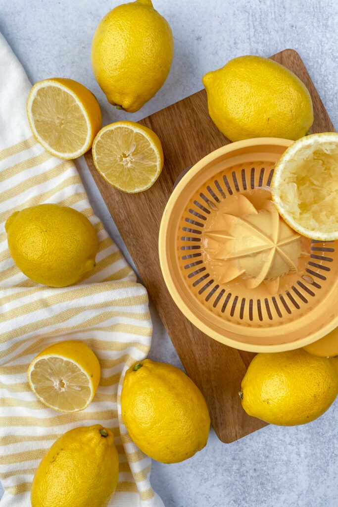 Eight lemons being squeezed by hand to make enough fresh lemon for a gallon of homemade lemonade.