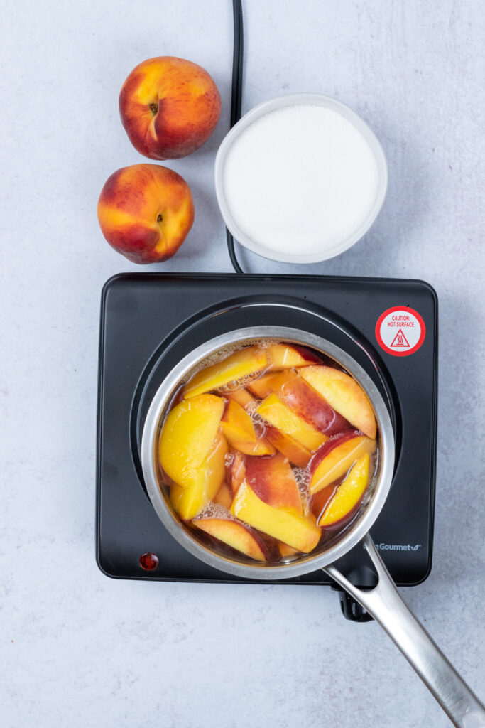 Peaches and water starting to boil in a saucepan on the stove, with bubbles forming around the edges.