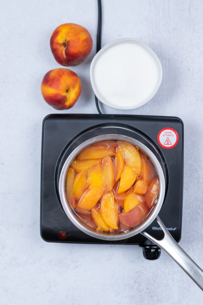 Overhead shot of simmering peaches as their color fades and the water takes on a peachy hue.