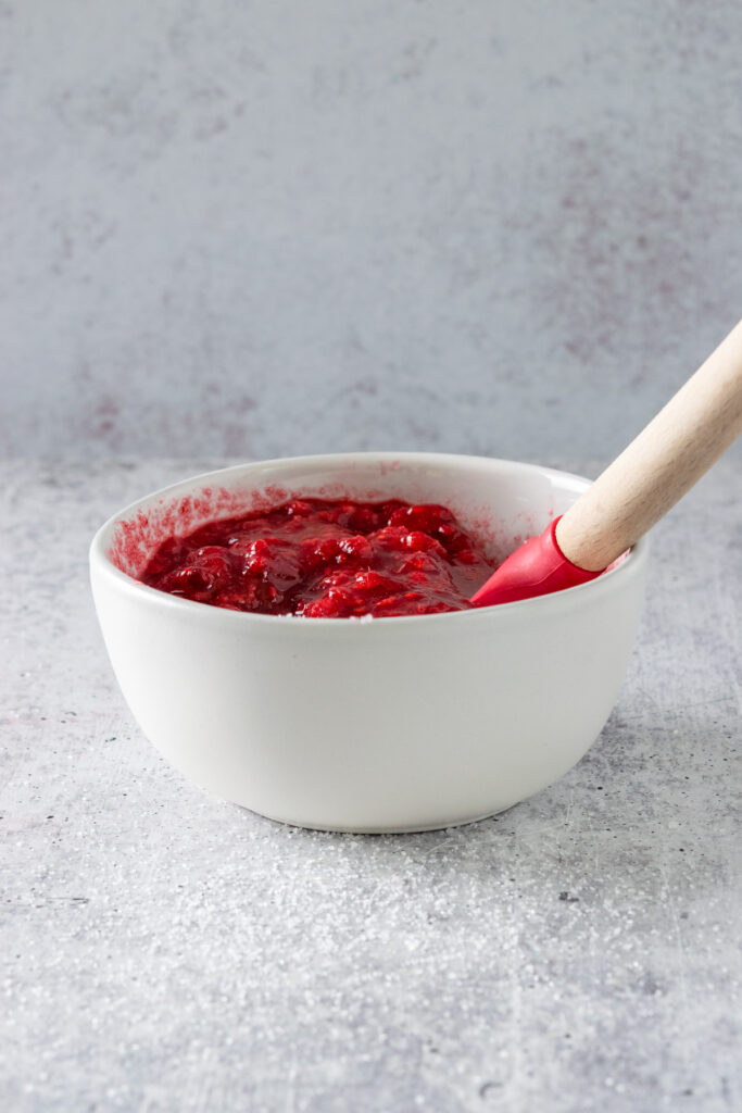 Juicy raspberries macerating in a bowl with a spoon in it.