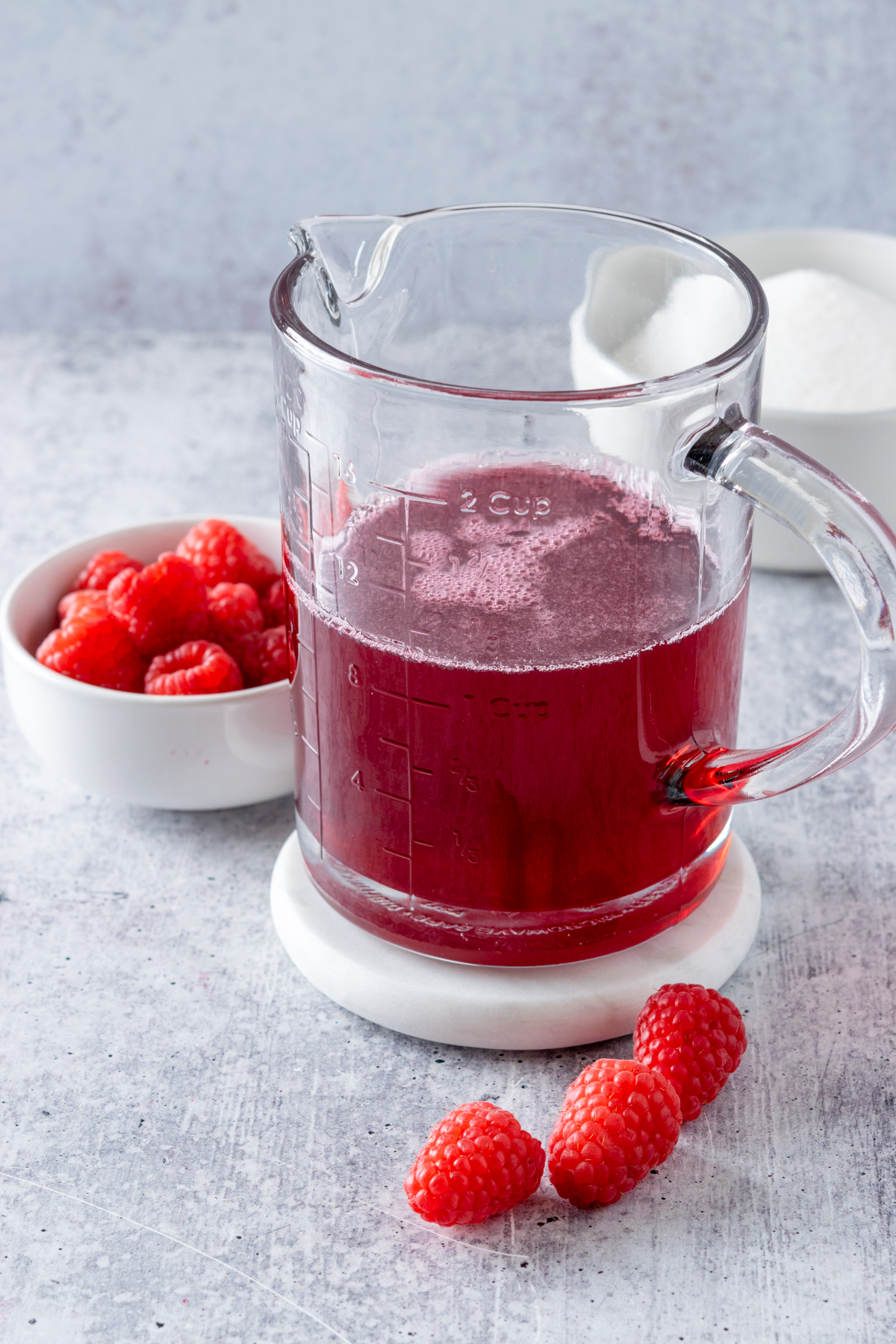 Jar of homemade raspberry syrup next to a small bowl of raaspberries.