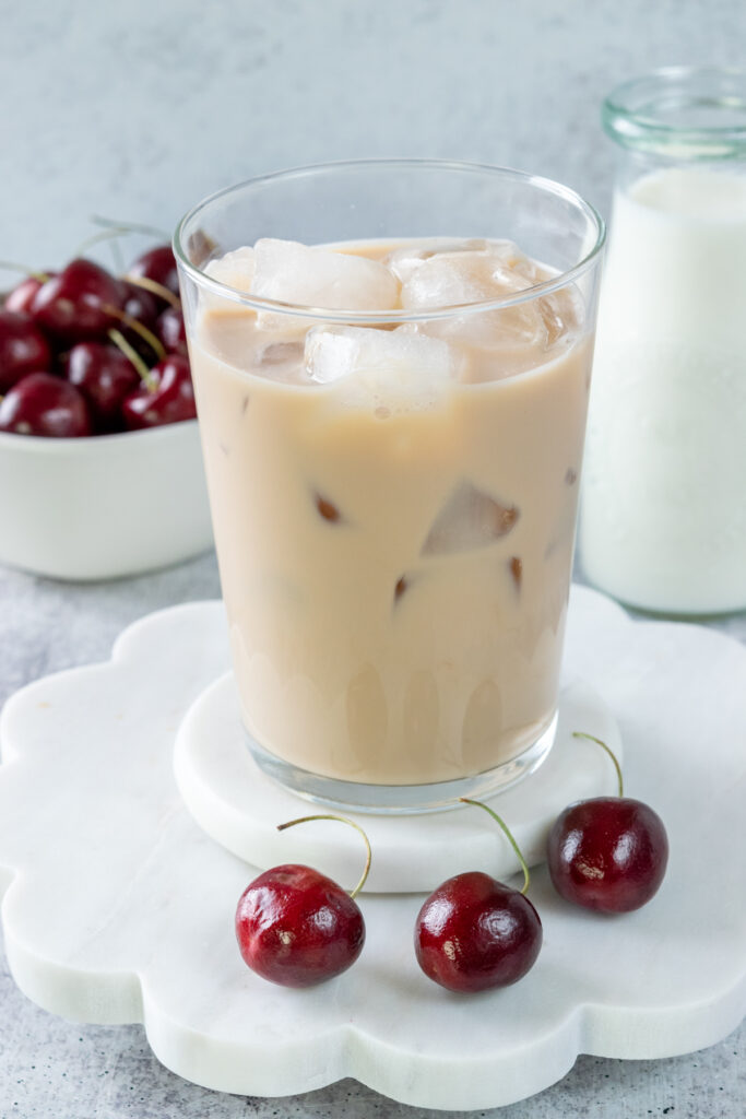 Ice is added to fill up the chai tea latte in a glass cup to make an iced cherry chai.