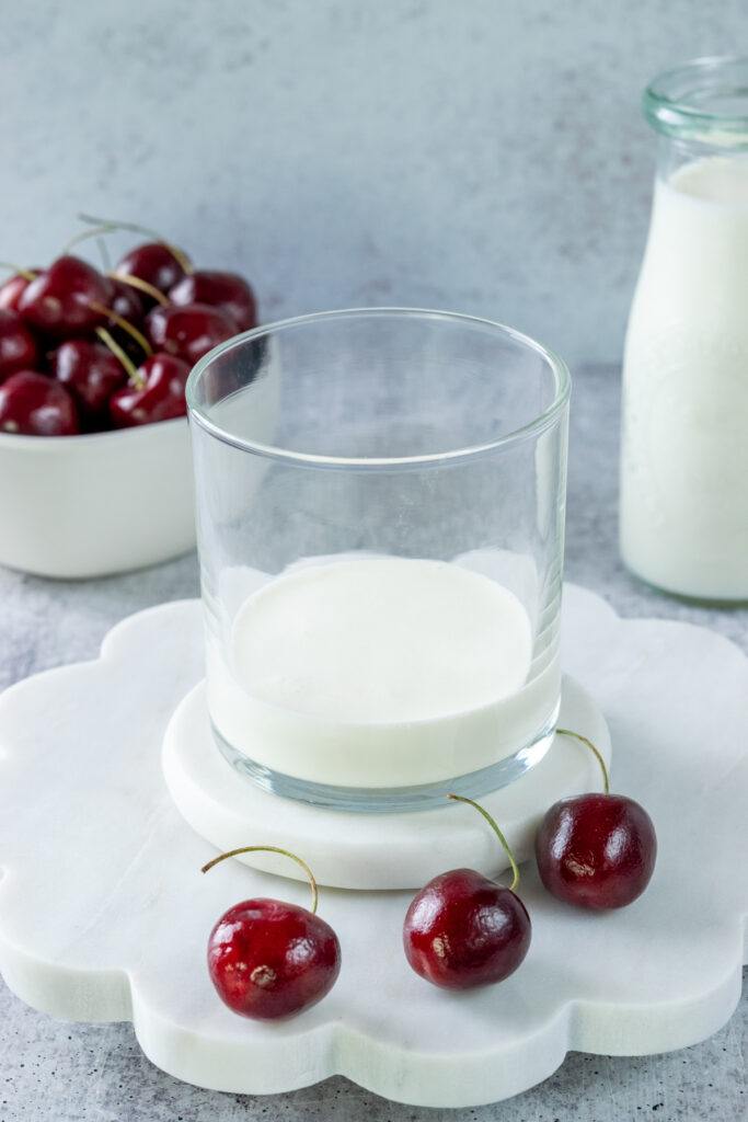 A small glass cup with a little bit of heavy cream and a splash of milk in it for making the cherry cold foam drink topping.