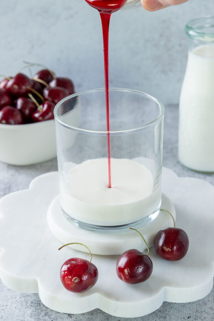 Cherry syrup being poured into glass of heavy cream and milk to make cherry cold foam.
