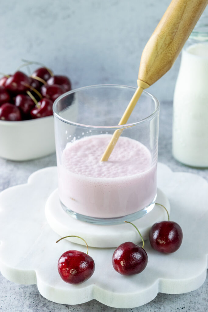 Cherry cold foam in a glass jar that's been frothed into a thick cream. The milk frothing wand is in the glass.