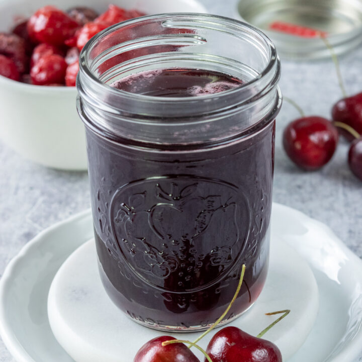 Jar of homemade cherry syrup next to a bowl of cherries.
