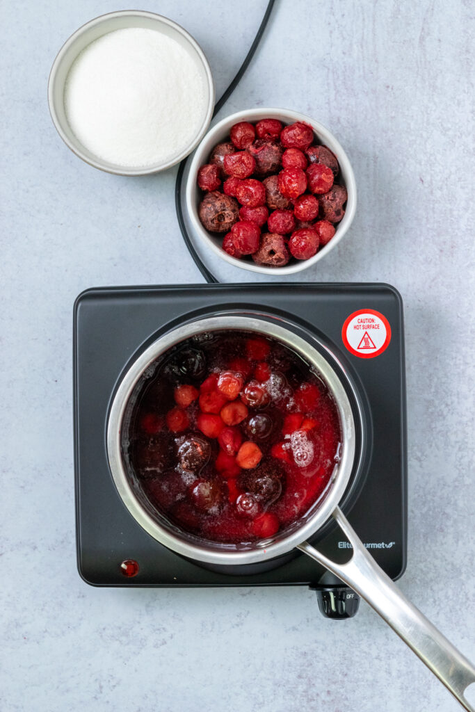 An overhead picture showing a saucepan full of cherries and water on a burner to make homemade cherry syrup.