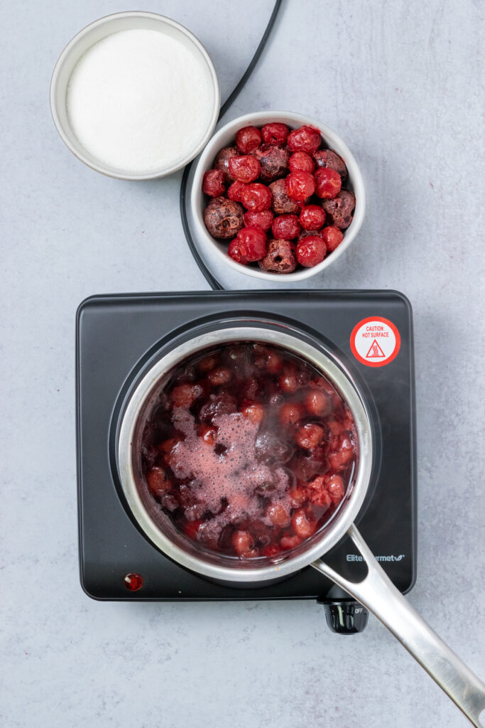 Boiling cherries and water in a saucepan on a burner to make cherry simple syrup.