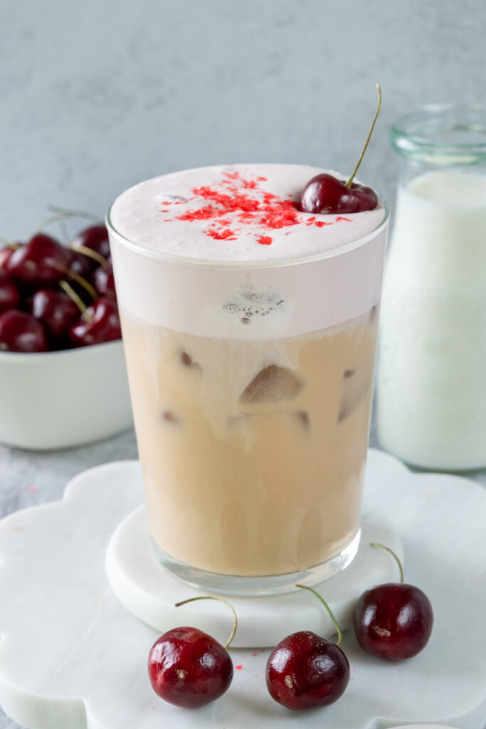 A homemade ice cherry chai drink topped with a layer of cherry cream cold foam and cherry candy sprinkles.