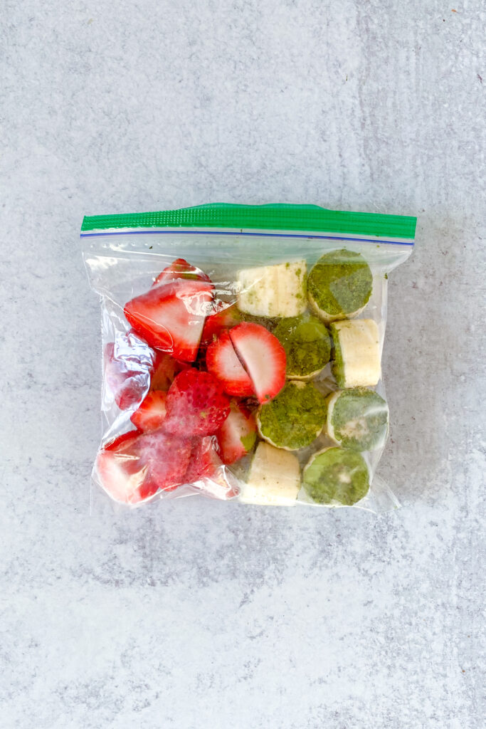 A plastic freezer bag filled with frozen strawberry halves and frozen banana dipped in matcha.