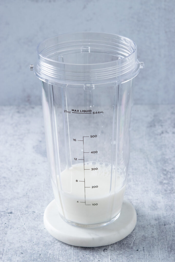 A blender cup with milk in it.