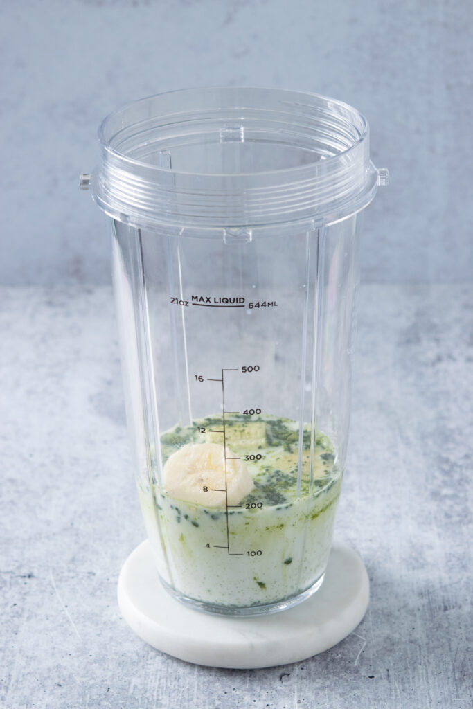 A blender cup with milk, matcha and banana in it.
