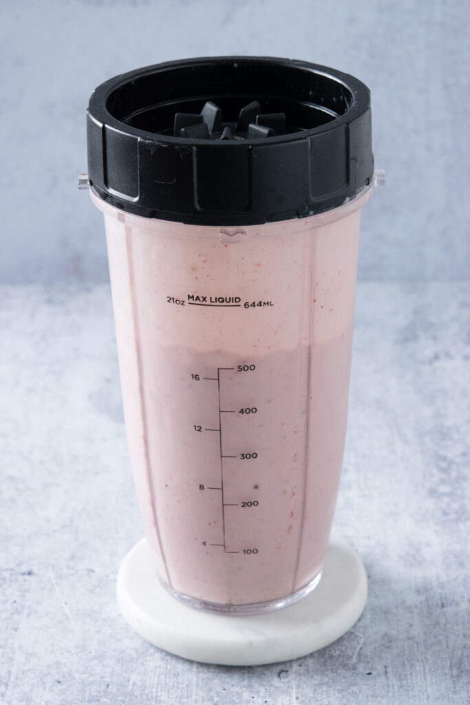 A strawberry matcha smoothie all blended in a blender cup with the lid on.