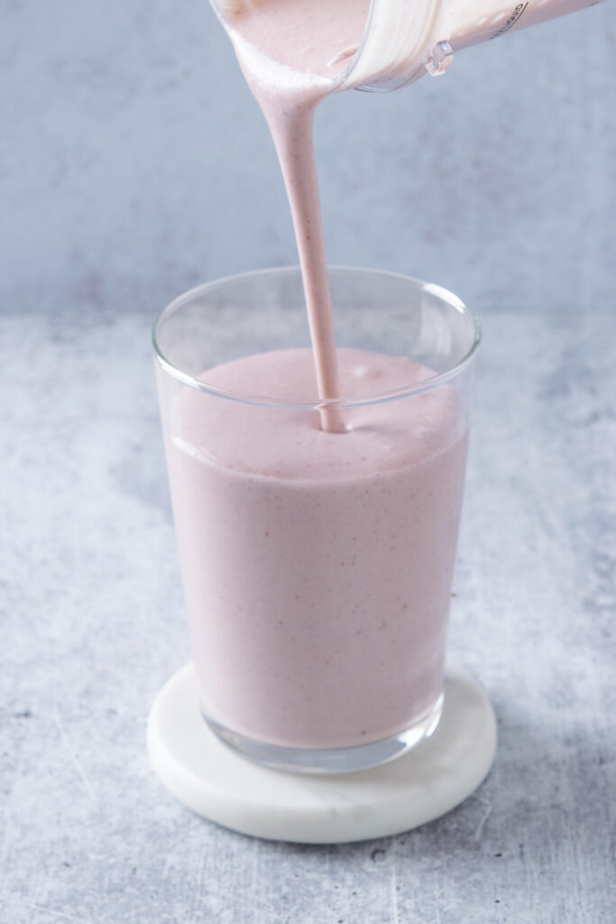 Pouring a blended strawberry matcha smoothie from the blender container into a glass.