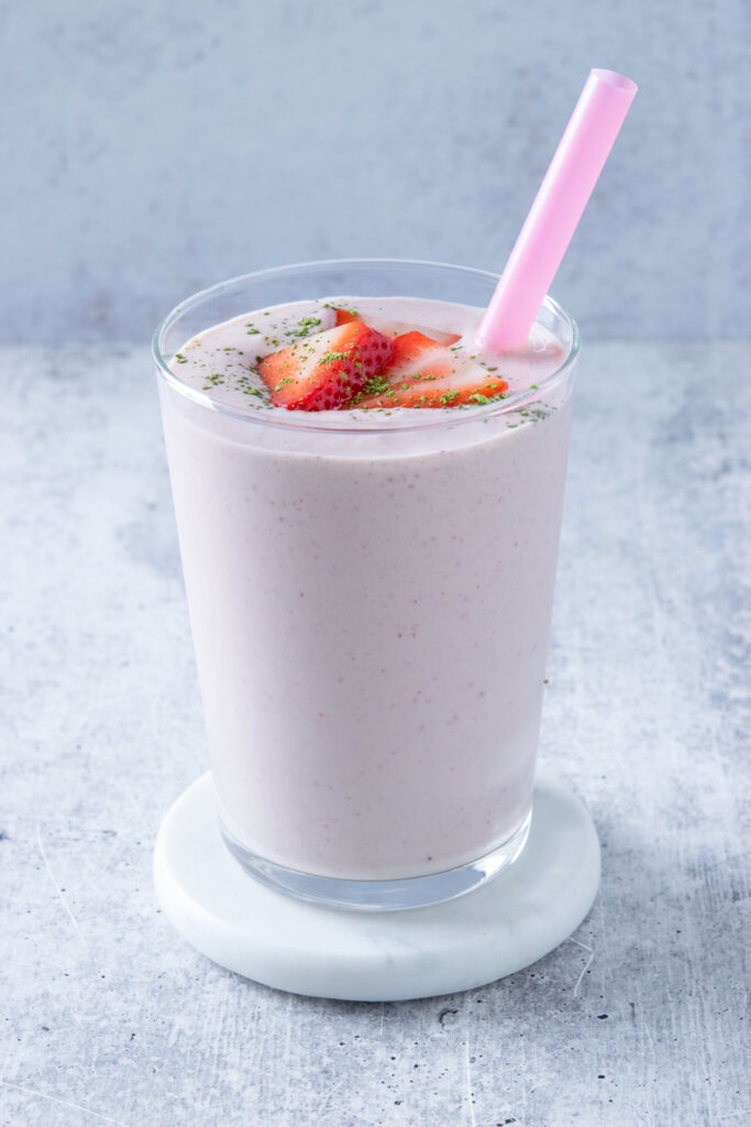 The strawberry matcha smoothie is garnished with strawberries and a little bit of matcha powder.