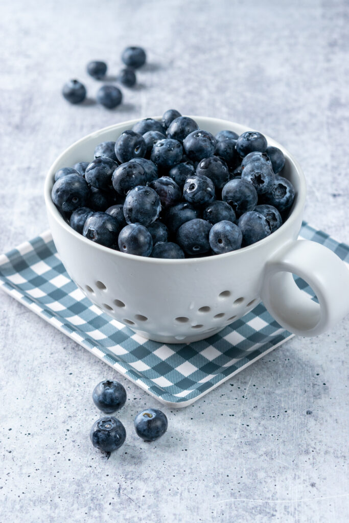 Wet blueberries in a berry bowl after rinsing. The berry bowl is on top of a blue checked plate.